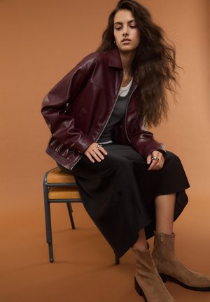 Giacca in pelle bordeaux con chiusura a zip, gonna nera in satin e stivaletti beige in suede. Tessuto liscio e design a vestibilità rilassata.