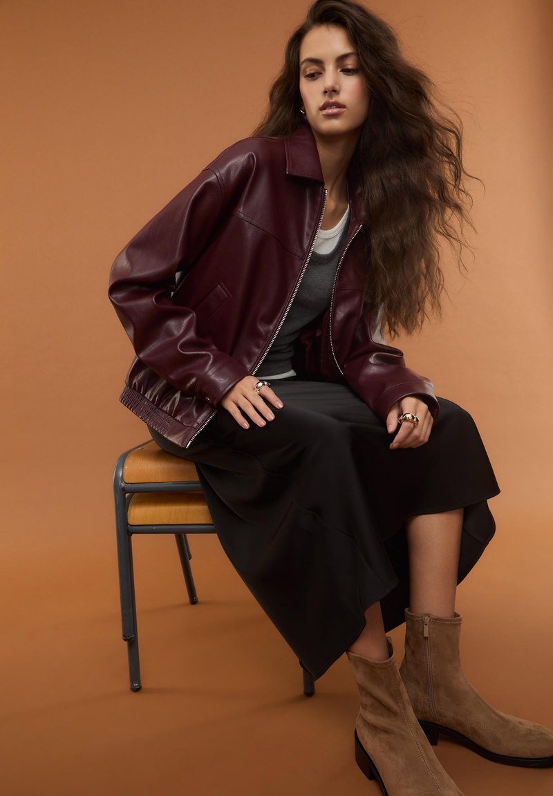 Giacca in pelle bordeaux con chiusura a zip, gonna nera in satin e stivaletti beige in suede. Tessuto liscio e design a vestibilità rilassata.