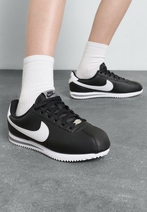 Les baskets Nike noires présentent une tige synthétique, un logo swoosh blanc, des lacets texturés et une semelle extérieure blanche contrastée avec un motif en zigzag.