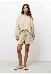 Beige loungewear set met een losse sweatshirt en shorts met koordjes, gemaakt van zacht materiaal, met een relaxte pasvorm en minimale ontwerpelementen.
