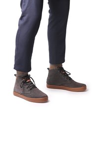 Zapatos de ante gris de caña alta con cordones negros, suelas de goma marrones y un acento texturizado en el tobillo, combinados con calcetines estampados.