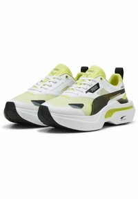 Sneaker bianchi e giallo neon con tomaia in mesh testurizzato, accenti verde scuro, suola nera e un design chunky distintivo.