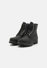 Botas de cuero negras hasta el tobillo con cuello acolchado, punta redonda, diseño de cordones y suela con relieve resistente. Presenta un detalle de logotipo en el lateral.