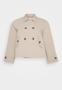 Beige dobbeltspent jakke med krage, to frontlommer og messingknapper. Har en kort lengde og strukturert stoff.