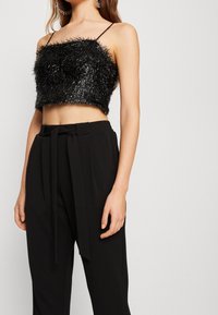 Haut court noir à texture duveteuse, réalisé en fil métallique, associé à un pantalon noir taille haute avec un détail de ceinture nouée.