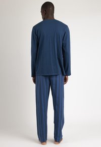 Camisa de manga larga en navy y pantalones de pijama a rayas en azul con finas líneas verticales. Tela suave, corte holgado y diseño simple.