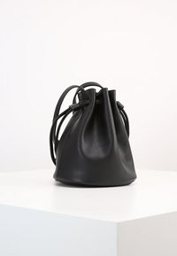 Borsa a secchiello in pelle nera con cima arricciata. Texture liscia, corpo arrotondato e due spallacci regolabili. Design semplice e minimalista.