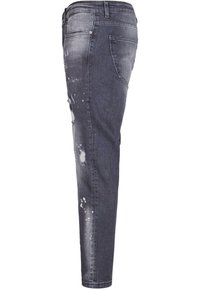 Jean slim gris foncé avec des zones déchirées et des éclaboussures de peinture blanche, présenté de profil avec une poche arrière visible et des passants de ceinture.