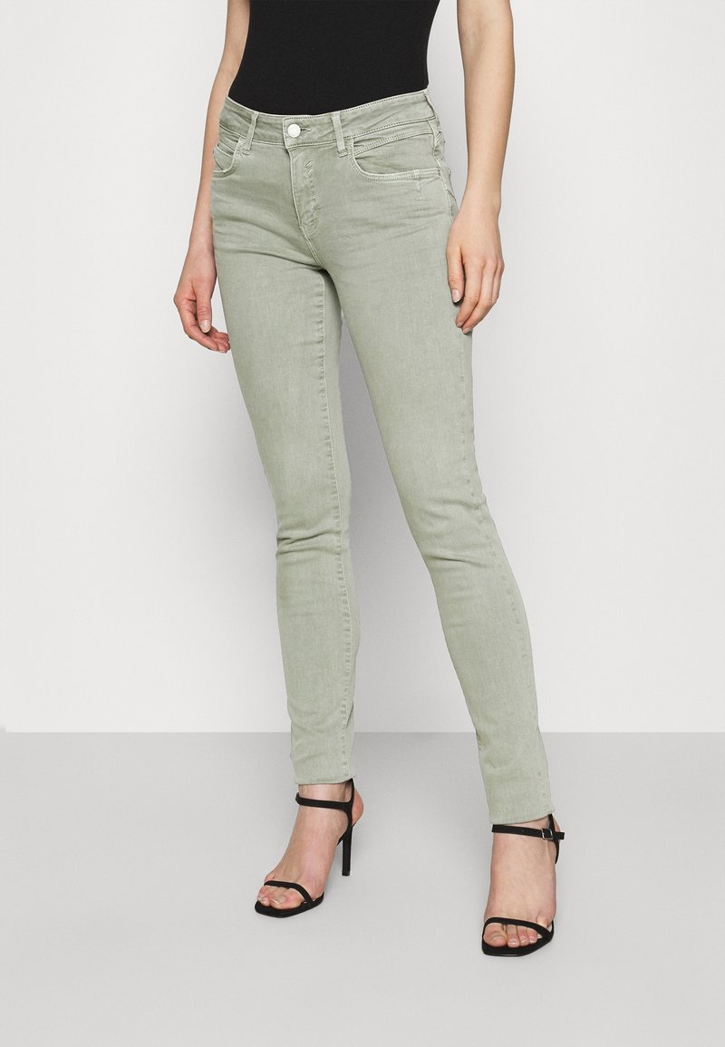 Jeans ajustados verde claro con una textura suave, que cuentan con bolsillos frontales y cremallera. Combinados con sandalias negras de tacón alto con tiras.