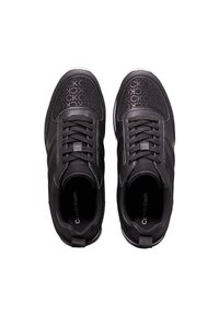 Zapatillas negras con un patrón de logo, parte superior sintética texturizada, diseño de cordones y una suela blanca en contraste.