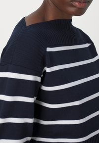 Maglione a righe navy con strisce orizzontali bianche, texture a coste sul colletto e una vestibilità leggermente rilassata.