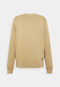 Sudadera marrón claro con cuello redondo, puños y bajo acanalados. Presenta un pequeño logo en el lado inferior izquierdo. Textura suave, diseño casual.