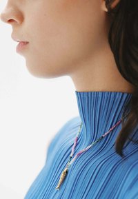 Top de punto plisado azul con un alto cuello. Llevado con un collar de cuentas multicolor que presenta un pequeño colgante. Textura suave y diseño ajustado.
