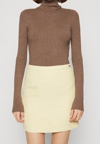 Bruine geribbelde coltrui gecombineerd met een korte, gestructureerde gele rok. Beide kledingstukken hebben een aansluitend ontwerp en minimale details.