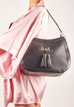 Borsa a mano in pelle nera con forma curva, accessori in oro e un accento con nappina. La borsa ha una texture liscia e una struttura robusta.