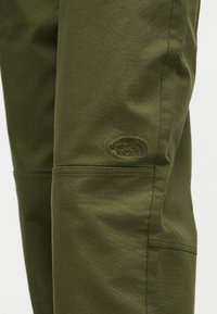 Παντελόνι ελιάς με ορατές ραφές και το λογότυπο της The North Face κεντημένο πάνω από το γόνατο στο αριστερό πόδι.