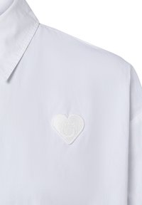 Weißes Hemd mit Kragen, das ein gesticktes herzförmiges Emblem mit dem Text "Hugo" auf der linken Brustseite zeigt.