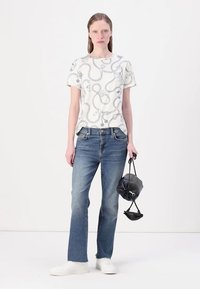 Hvid t-shirt med grå, flydende mønster; blå lige jeans; hvide sneakers; holder en lille, rund, mørk taske. Minimalistisk design.