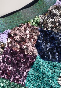 Tissu à paillettes multicolores avec différentes nuances de vert, bleu, violet et cuivre. Présente une surface texturée et réfléchissante avec des paillettes circulaires.