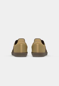 Braune und beige Sneakers mit einer strukturierten Oberseite, niedrigem Profil und einer Gummisohle mit gemustertem Profil für besseren Halt.