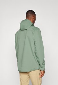 Hooded jacket in muted green, featuring a smooth texture and a relaxed fit. Visible stitching and subtle accents at the hem and sleeves.