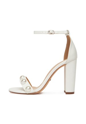 Fehér magassarkú szandál bokapánttal, három nagy gyöngy díszítéssel a felső pánton és masszív blokk sarkon. Simább textúra.
