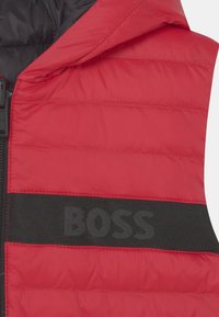 Red puffer vest with a black zipper, featuring horizontal quilting and a prominent black band with the text "BOSS" displayed in dark gray.