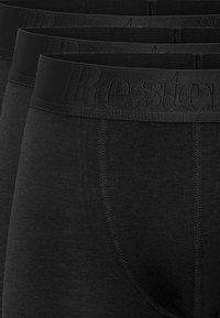 Boxer in cotone nero con una fascia elastica che presenta il nome del brand in rilievo. Sono visibili dettagli di cucitura e una texture liscia.