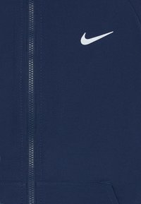 Marinblå zip-up hoodie i texturerat tyg, med en central dragkedja och en vit Nike-logga på övre vänstra sidan.