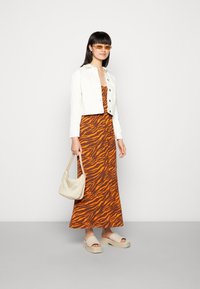 Jaqueta de ganga branca cortada sobre um vestido maxi listrado de tigre laranja e castanho, combinado com sandálias de plataforma cremosas e uma bolsa bege.