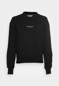 Sudadera negra de algodón, con cuello redondo y mangas largas. En la parte frontal se muestra un logo blanco de Calvin Klein Jeans.