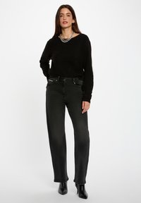 Maglione nero oversize in maglia, abbinato a jeans scuri a vita alta. Tessuto morbido, accenti minimali e taglio alla caviglia con gamba leggermente affusolata.