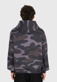 Person set fra bagfra iført en grå og sort camouflagehætte sweatshirt med lange ærmer.