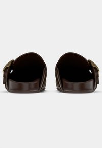 Brune slidssandaler med bred rem, med en guldfarvet metaldekoration, glat tekstur og åben tå-design.