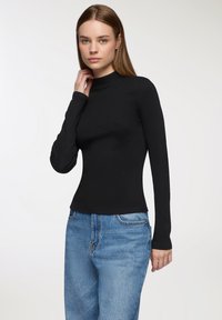 Czarna, długozasłonowa bluzka z wysokim kołnierzem, wykonana z prążkowanej tkaniny. W połączeniu z jasnoniebieskimi dżinsami o klasycznym kroju i lekkim wyblaknięciu.