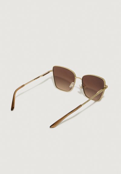 Óculos de sol com tonalidade castanha, com forma geométrica, armação em metal dourado, detalhes texturizados na parte superior e hastes finas em plástico castanho.