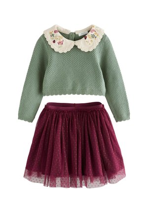 Grüner gestrickter Pullover mit gewelltem weißen Kragen und Blumenstickerei, kombiniert mit einem burgunderfarbenen Tüllrock mit Punkten.