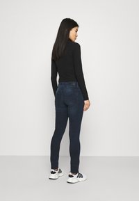 Mørkeblå skinny jeans med høy livhøyde og subtile baklommer, kombinert med en tettsittende svart langermet topp og svart-hvite sneakers.