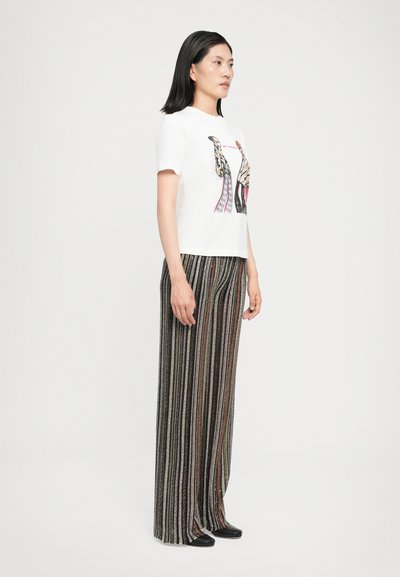 T-shirt en coton blanc avec un design imprimé coloré, associé à un pantalon large noir à rayures avec des lignes multicolores et une texture.