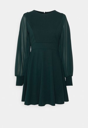 Rochie skater de culoare verde închis, cu un corp ajustat, decolteu rotund și mâneci balloon din material transparent. Prezintă o fustă evazată și închidere cu fermoar la spate.