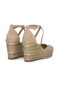 Sandali con zeppa in suede beige, con cinturini incrociati alla caviglia, caratterizzati da una finitura in juta intrecciata e accenti metallizzati su un tacco a zeppa texturizzato.