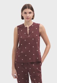 Top sans manches bordeaux avec un col rond, présentant une fente verticale et des motifs en forme de diamant de couleur crème sur un tissu texturé.