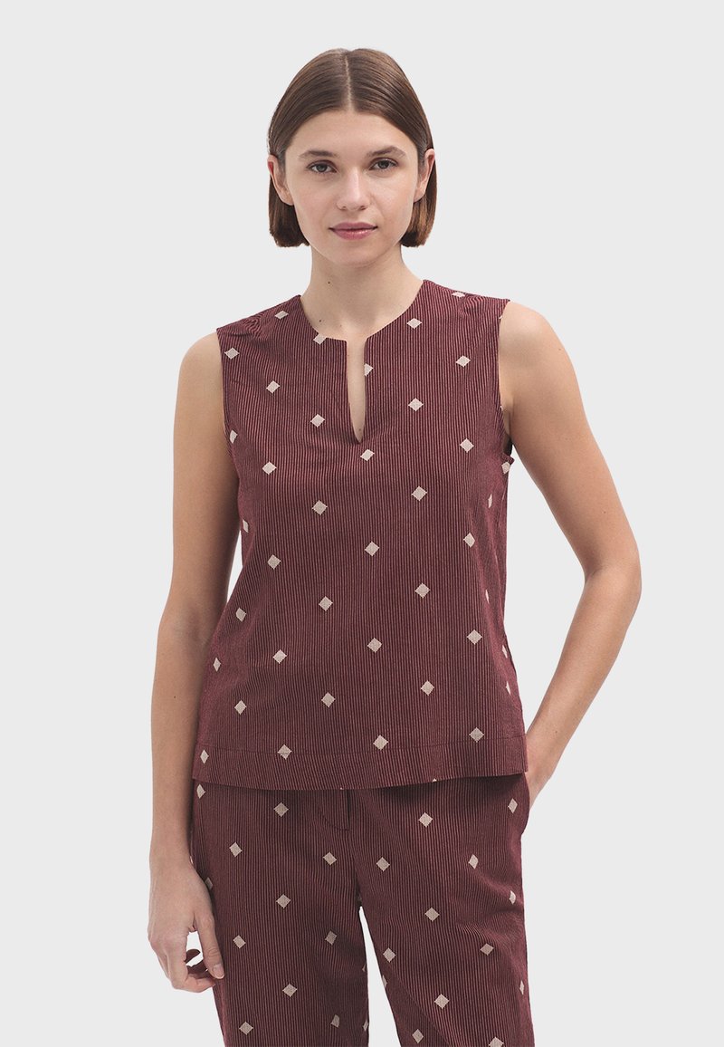 Top sans manches bordeaux avec un col rond, présentant une fente verticale et des motifs en forme de diamant de couleur crème sur un tissu texturé.