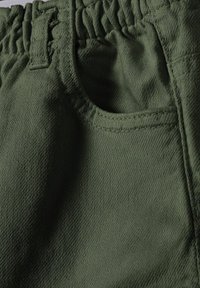 Gröna tygshorts med elastiskt midjeband, utrustade med en sidoficka och texturerad yta. Materialet verkar hållbart och mjukt.