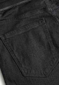 Tejido de mezclilla negro con un bolsillo trasero y costuras bordadas en un patrón curvado. La tela tiene una textura suave con sutiles brillos.