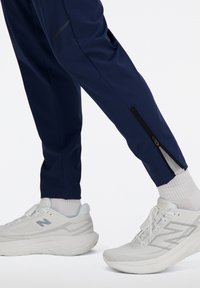 Marine sportbroek met zijrits, gecombineerd met witte sneakers met een gaasontwerp en een schokabsorberende zool. Gevarieerd geweven stof getoond.