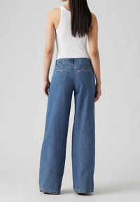 Breda blå denim jeans med medelhög midja, som har två bakfickor och en subtil logotyp på midjeresåren. Texturerad tyg.