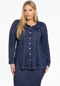 Donkerblauw denim overhemd met lange mouwen, goudkleurige knopen en een licht gebogen kraag. Verticale stiksels zorgen voor structuur.