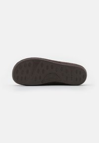 Suela de goma marrón con suelas circulares, que presenta una superficie texturizada y una marca sutil, diseñada para ofrecer agarre y durabilidad.