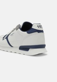 Weiße und marineblaue Sneaker mit einem strukturierten Lederoberteil, grauen Akzenten und einer gepolsterten Sohle. Mit Markenlogo und "1973"-Detail an der Ferse.